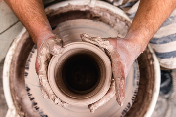 Fototapeta na wymiar Top view of potter's hand making a vase of white clay on throwing-wheel in ceramics studio, concept of creativity and art, horizontal photo, selective focus