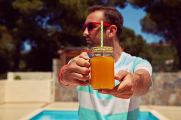 Attractive man drinking juice on the swimming pool. Summer concept.