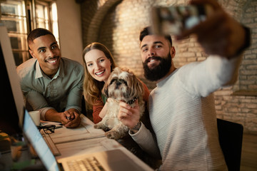 Group of happy colleagues taking selfie with a dog in the office.