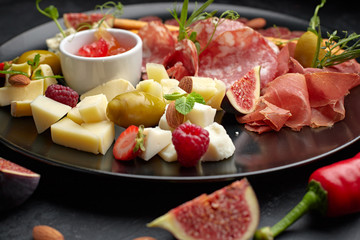 Meat and cheese assorted, on a black plate with herbs and berries