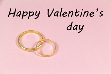 Two wedding rings and happy Valentine's day on pink background