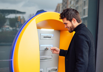 Young man with attractive beard takes money from an ATM.