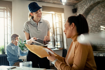 Happy courier giving touchpad to a female customer to sign for a delivery.