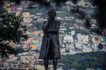 Fototapeta na wymiar Statue on boulevard 24 de mayo square in Quito, Ecuador on a february midday. Houses of quito are seen in the distance in the background.