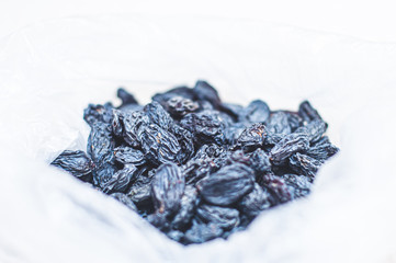 Black dried raisins in a plastic bag on a white table. The rate of dried blue grapes for an adult. Dried fruits