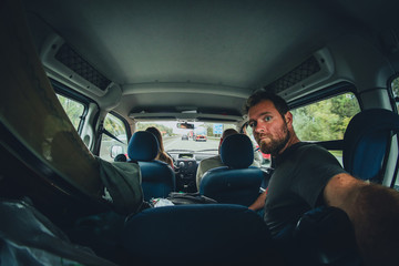 Three people riding in a minivan with loaded skis, going on a trip. One person is holding a camera...