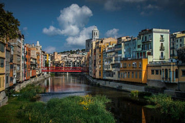 Fototapeta na wymiar Panorama of Girona from the river, with Girona cathedral of Saint Mary and red Eiffel bridge seen in the foreground. Greenery on the water is seen.