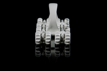 White plastic massager with wheels isolated on black with reflection on the bottom. Side and front view of plastic vintage roller massager.