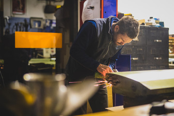 A young male is using an angle grinder on a vintage car door in a home workshop. Concept of working...