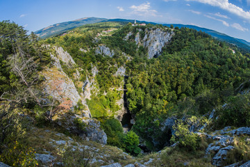 Unesco world heritage site Skocjanske jame taken with a wide fish eye view. Looking towards the deep gorge with cave entrance and walking paths. Village of Skocjan in the background.