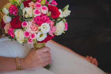 Arm of a woman holding a beautiful wedding bouquet made of red pink and white flowers, mostly roses. Other hand is seen holding a groom. Focus on the roses.