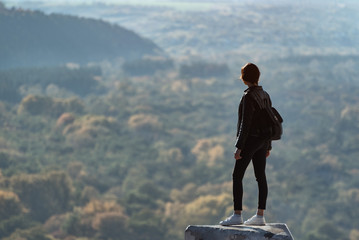 Girl stands on a hill and looks into the distance of the forest.