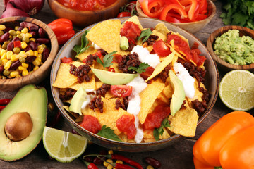 mexican nacho chips garnished with ground beef, guacamole, melted cheese, peppers and cilantro leaves in plate