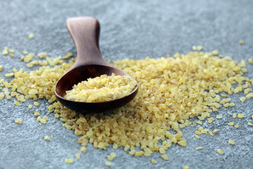 Uncooked bulgur in wooden spoon, rustic style. Healthy Bulgur wheat grains