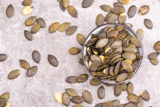 Pumkin seeds in a bowl on a grey textured background, empty copy space