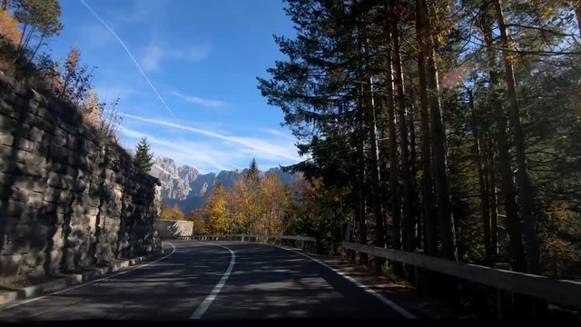 Inside car dashboard point of view forward moving driving on Slovenia road in valley between Alps and colorful trees with view of Mangart mountains in background