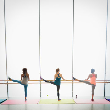 Women stretching legs at barre in exercise class gym studio