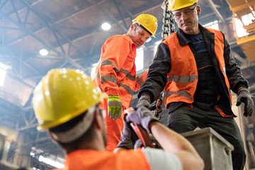 Steel workers fastening crane hook to steel in factory