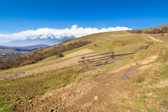rural landscape in spring. composite landscape of mountain ridge in the distance with snow capped tops and fields with fence along the country dirt road. warm sunny weather