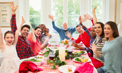 Portrait enthusiastic multi-ethnic multi-generation family waving at Christmas dinner table