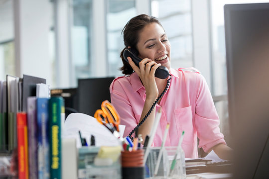 Smiling businesswoman talking on telephone working at computer in office