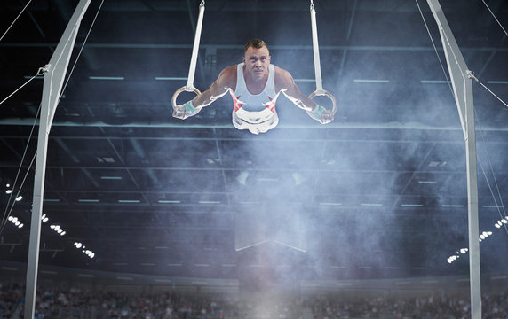 Male gymnast performing on gymnastics rings in arena