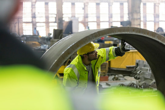 Steel worker examining pipe in factory