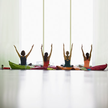 Women on cushions with arms raised in restorative yoga gym studio