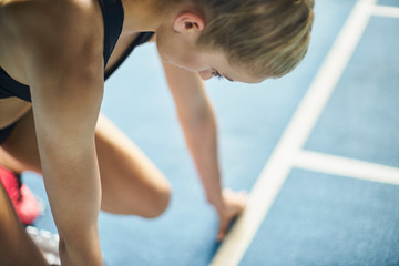 Focused female runner ready at starting block on sports track