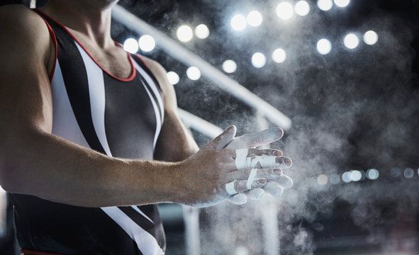 Male gymnast rubbing chalk powder on hands below parallel bars
