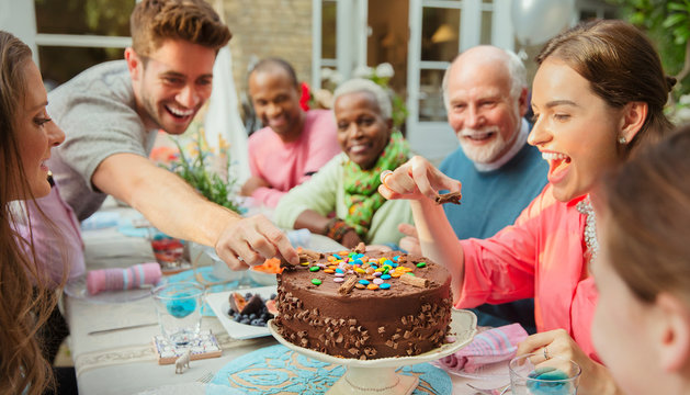 Family reaching for candy on chocolate birthday cake at patio table