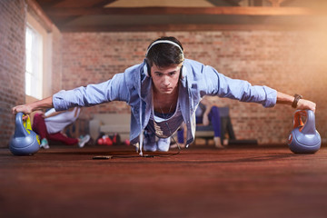 Focused young man balancing practicing plank pose on kettlebells in gym studio