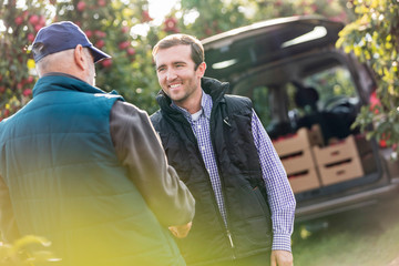 Smiling male farmer and customer handshaking in apple orchard