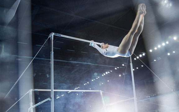 Female gymnast performing on uneven bars in arena