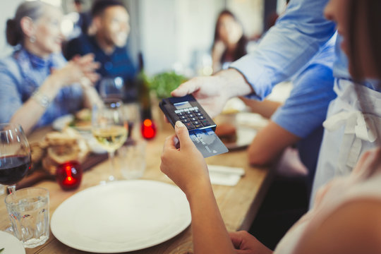 Woman credit card paying waiter, using credit card reader at restaurant table