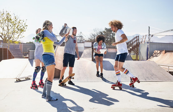 Friends roller skating and skateboarding at sunny skate park