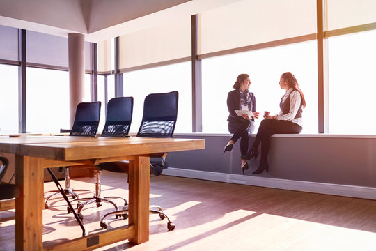 Businesswomen talking drinking coffee at sunny conference room window