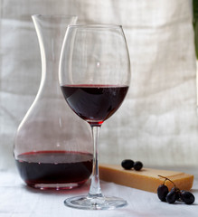 One glass with red wine, carafe with wine, cheese and grapes on a white background