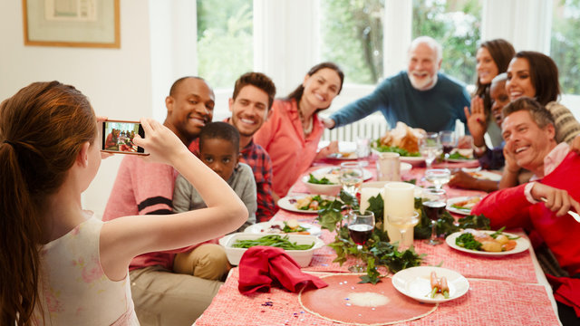 Girl camera phone photographing multi-ethnic family at Christmas dinner table