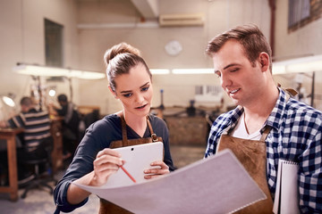 Jewelers with digital tablet and blueprints in workshop