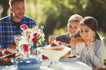 Father watching daughters eating at sunny garden party patio table