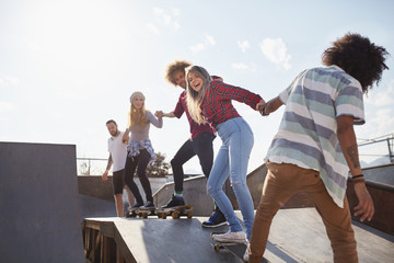 Friends on skateboards holding hands in a row on ramp at sunny skate park