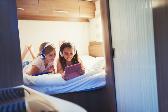 Sisters headphones sharing digital tablet, watching video inside motor home