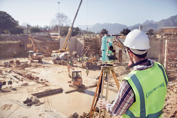 Construction worker surveyor using theodolite at sunny construction site