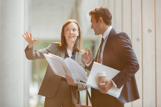 Businesswoman explaining paperwork to businessman in office lobby