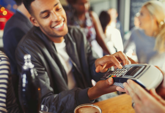 Smiling man paying bartender using credit card reader at bar