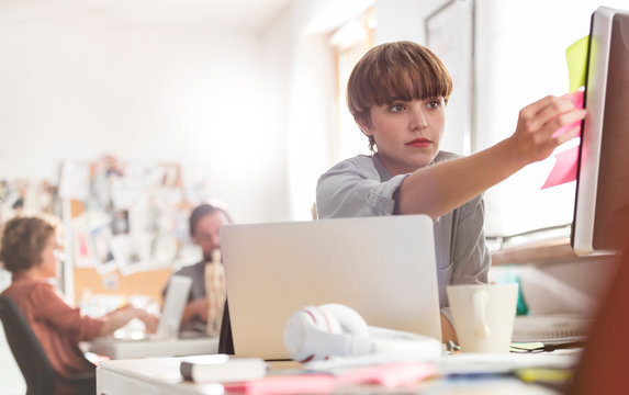 Serious female designer reviewing adhesive notes on computer in office