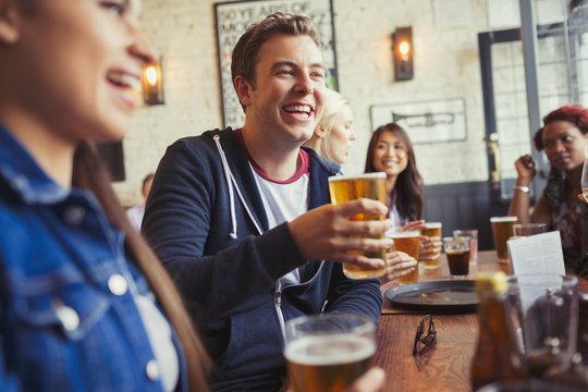 Smiling man drinking beer with friends at table in bar