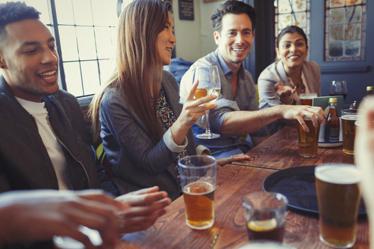 Friends drinking beer and wine and talking at table in bar