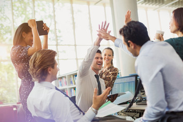 Business people high-fiving and celebrating in office